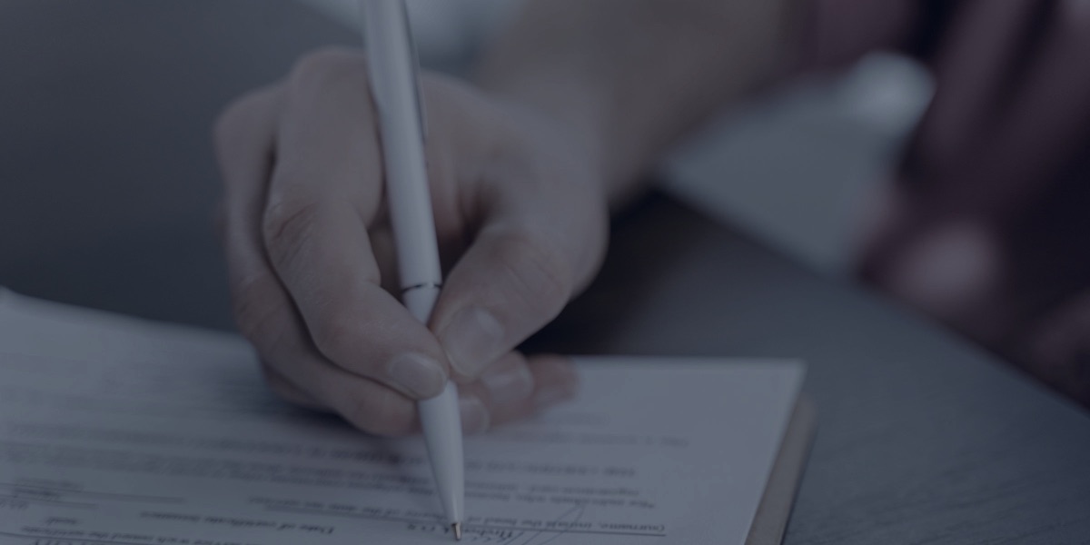Close de uma mão assinando um documento sobre a mesa