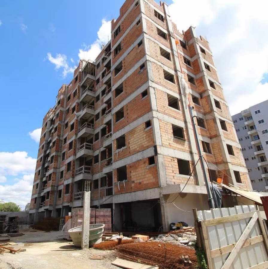 Prédio residencial de vários andares com a obra inacabada: estrutura de concreto e alvenaria aparente, vãos de janela sem esquadria, entulho e tapume de madeira no térreo, sem nenhuma atividade.